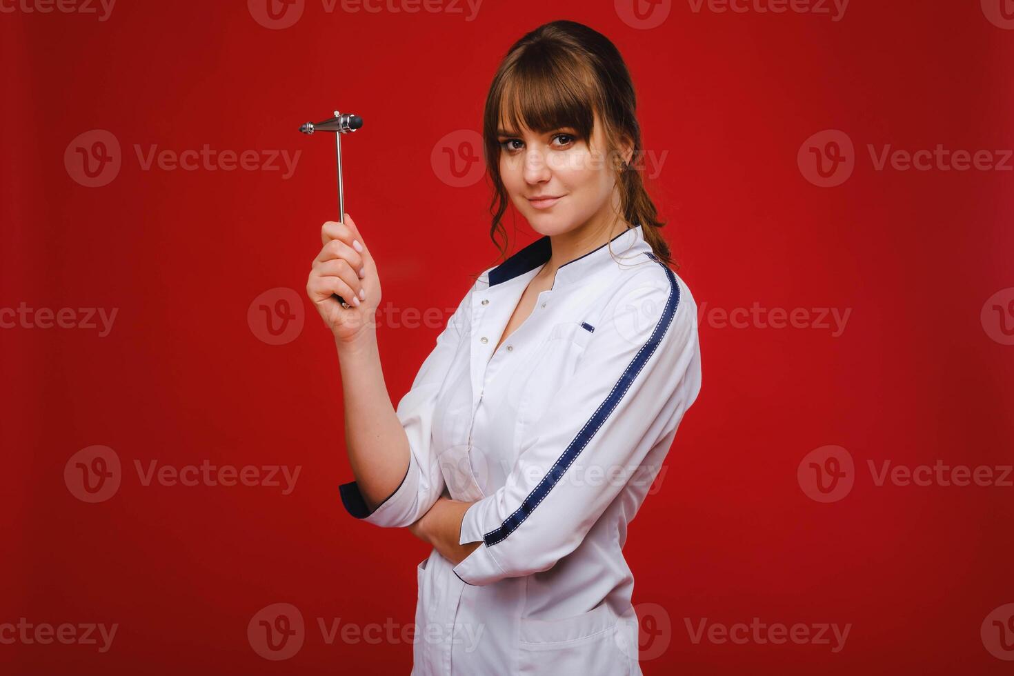 The doctor is holding a neurological hammer on a red background. The neurologist checks the patient's reflexes with a hammer. Diagnostics, healthcare, and medical care photo