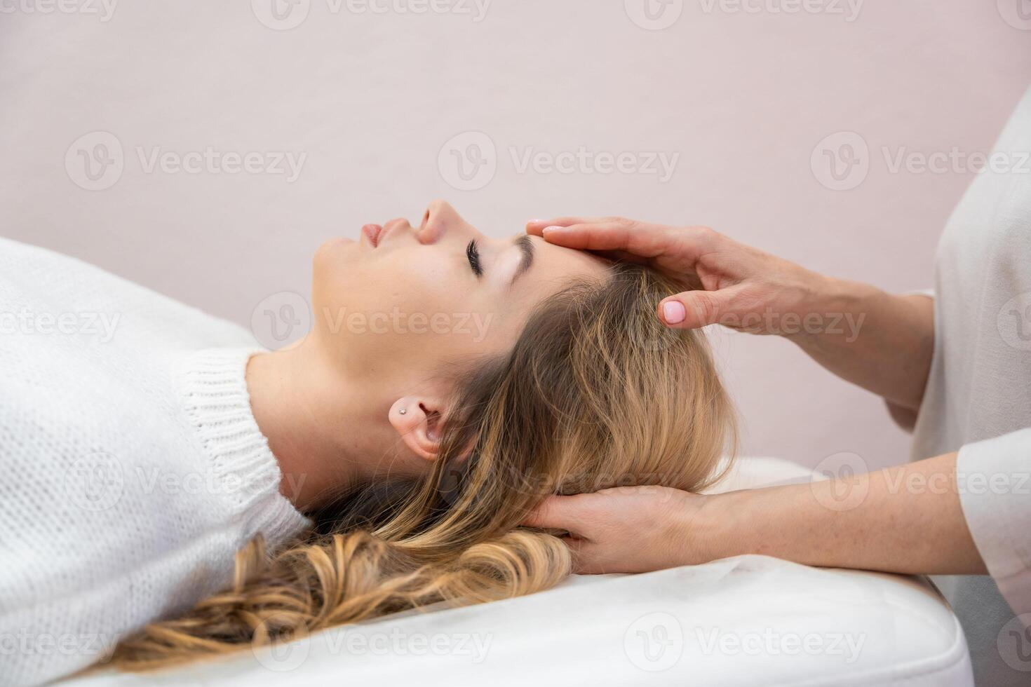 Healer performing set of 32 points of access bars on young woman head, stimulating positive change thoughts and emotions in salon. Alternative medicine photo