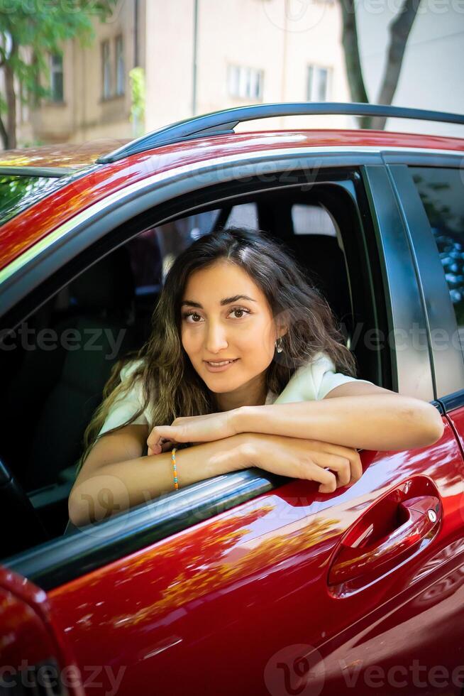 Happy smiling woman driver behind the wheel red car. View through car window photo