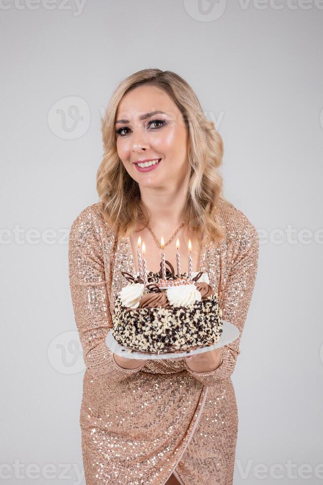 Pretty sexy blonde woman on white background. Portrait of beautiful young lady in beige glitter sequins long evening dress with cake and candles photo