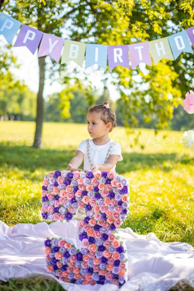 Cheerful girl having fun on child birthday on blanket with paper decorations in the park photo