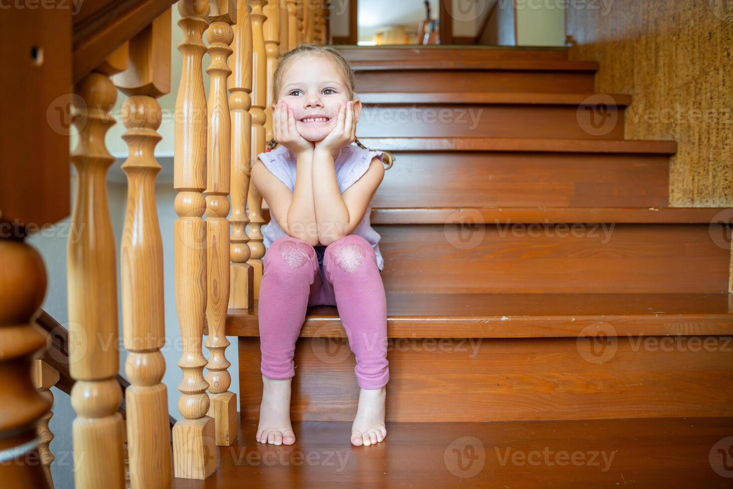 Happy little girl is sitting on stairs at home. Dangerous situation at home. Child safety concept. photo