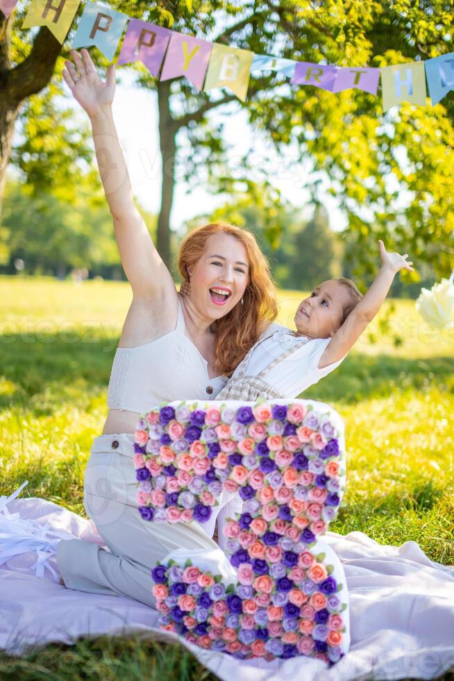 alegre madre y hija teniendo divertido en niño cumpleaños en cobija con papel decoraciones en el parque foto