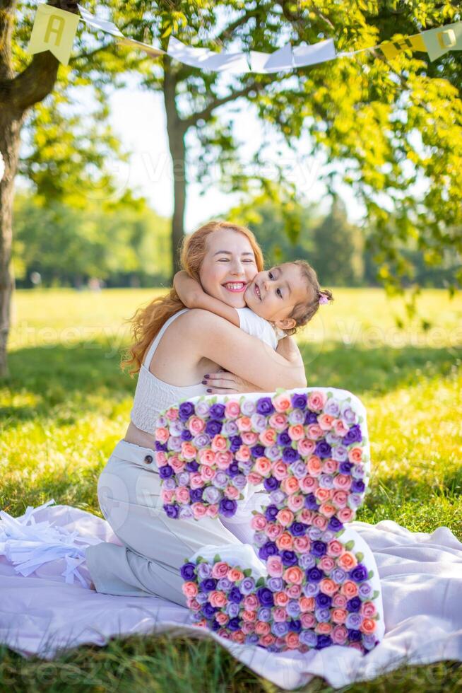 alegre madre y hija teniendo divertido en niño cumpleaños en cobija con papel decoraciones en el parque foto