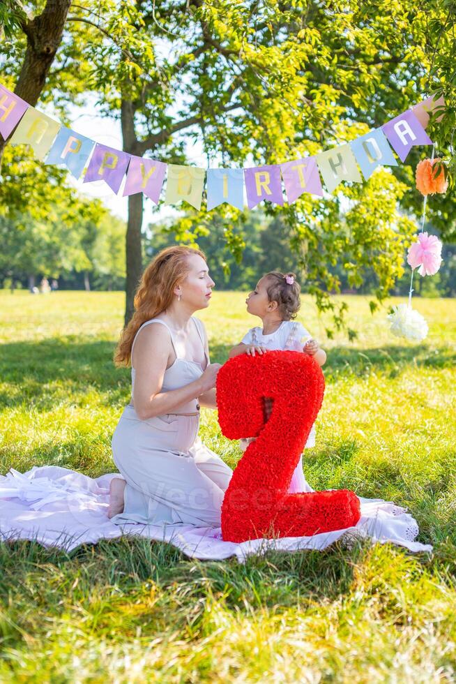 alegre madre y hija teniendo divertido en niño cumpleaños en cobija con papel decoraciones en el parque foto