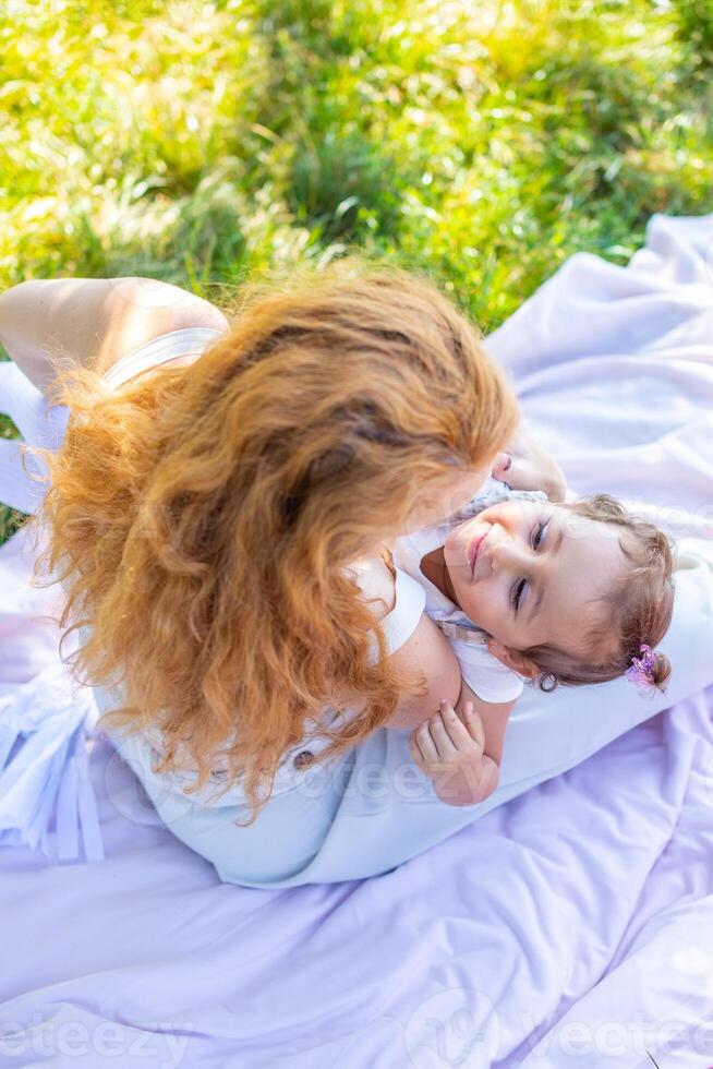 mamá y hija riendo y abrazando sentado en un cobija en el parque el concepto de un contento familia, amistad, y amor. foto