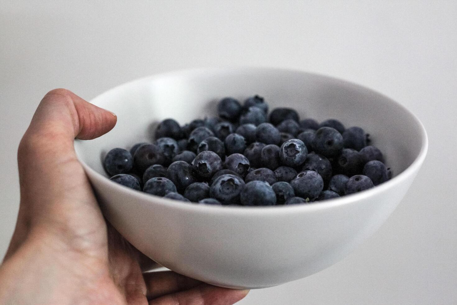 Hand holds a bowl of blueberry White cup of fresh berries in the hand. Close up photo