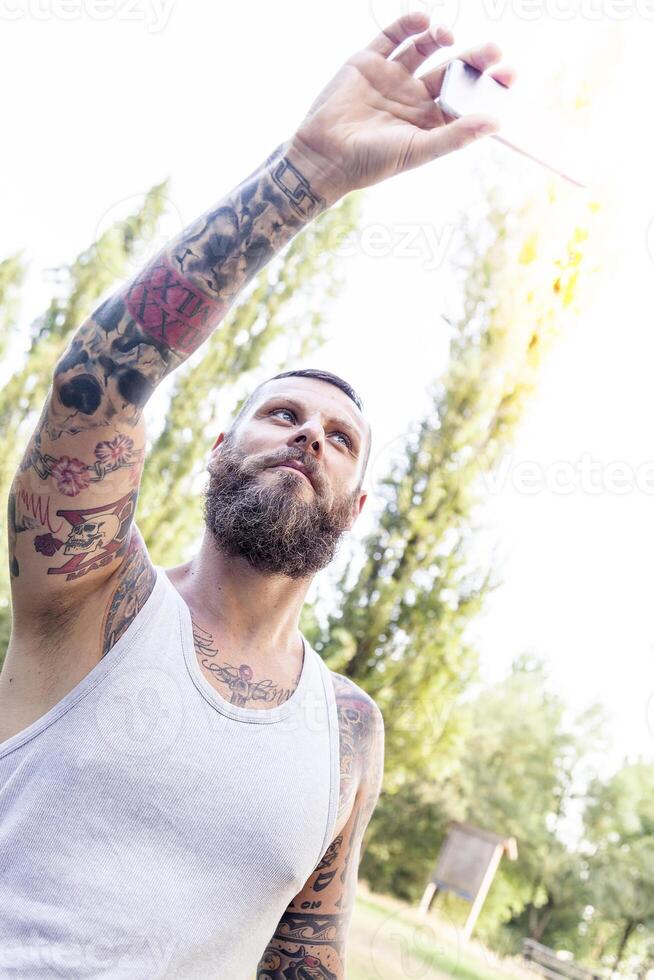 tattooed bearded man takes a selfie in the park photo