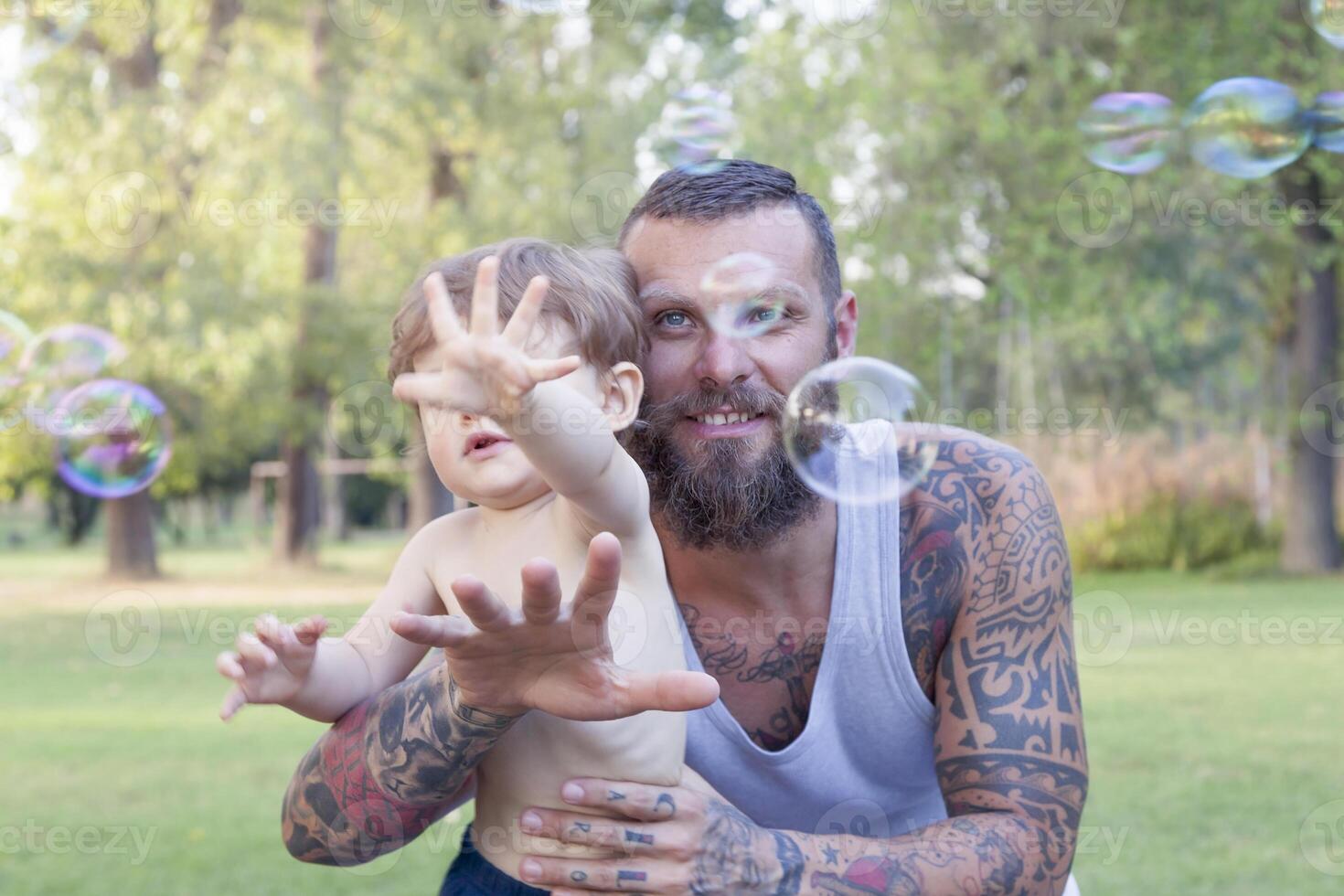 niño teniendo divertido con su papá y intentos a tomar jabón burbujas foto