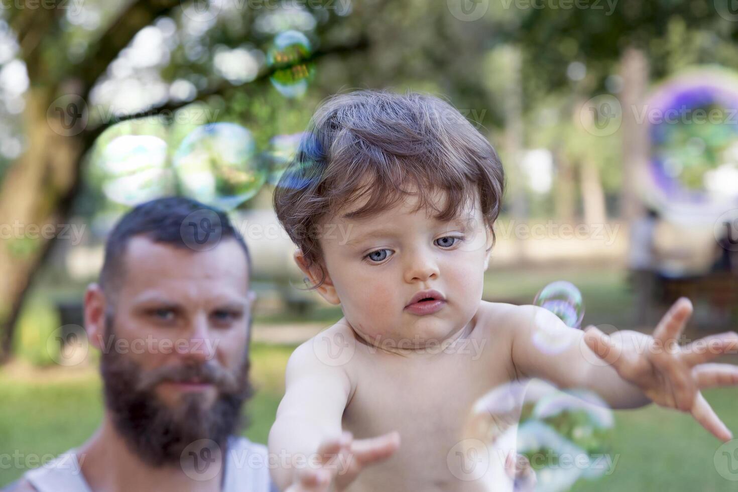 child having fun with his dad and tries to take soap bubbles photo