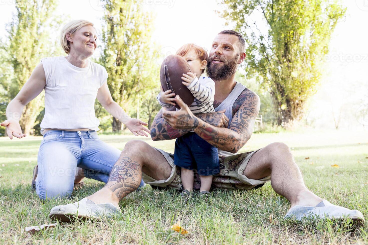 young couple with child having fun at the park with rugby ball photo