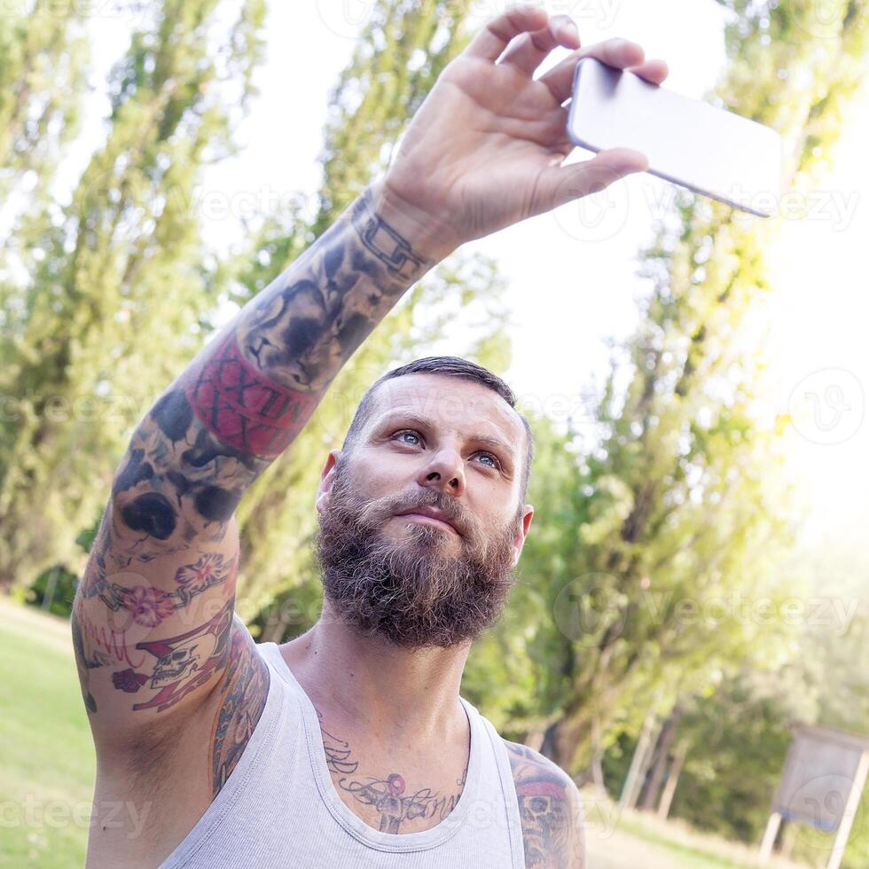 tattooed bearded man takes a selfie in the park photo