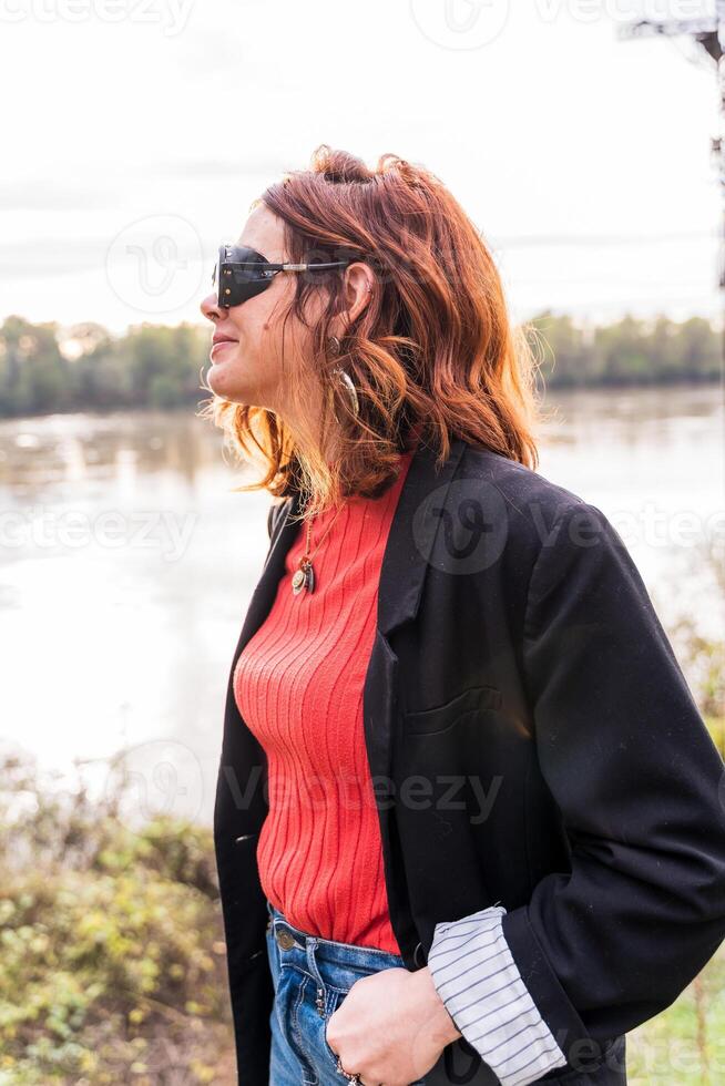 portrait of young adult red-haired woman outdoors on the river bank photo