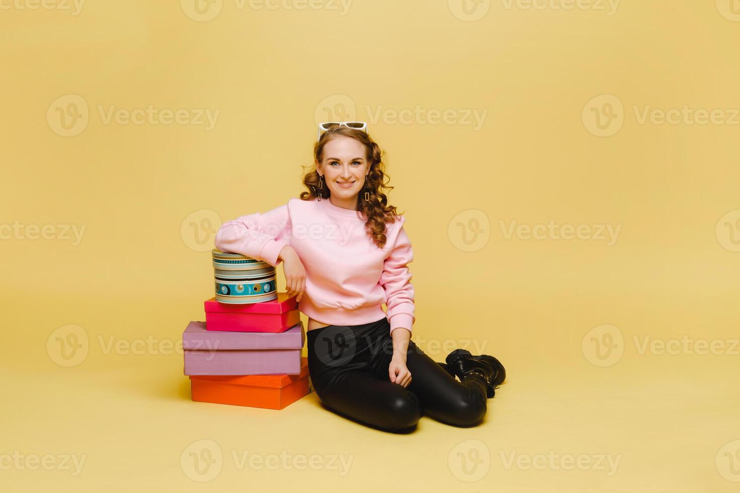 A happy young woman with colorful paper boxes after shopping isolated on an orange Studio background. Seasonal sales, purchases, spending money on gifts photo