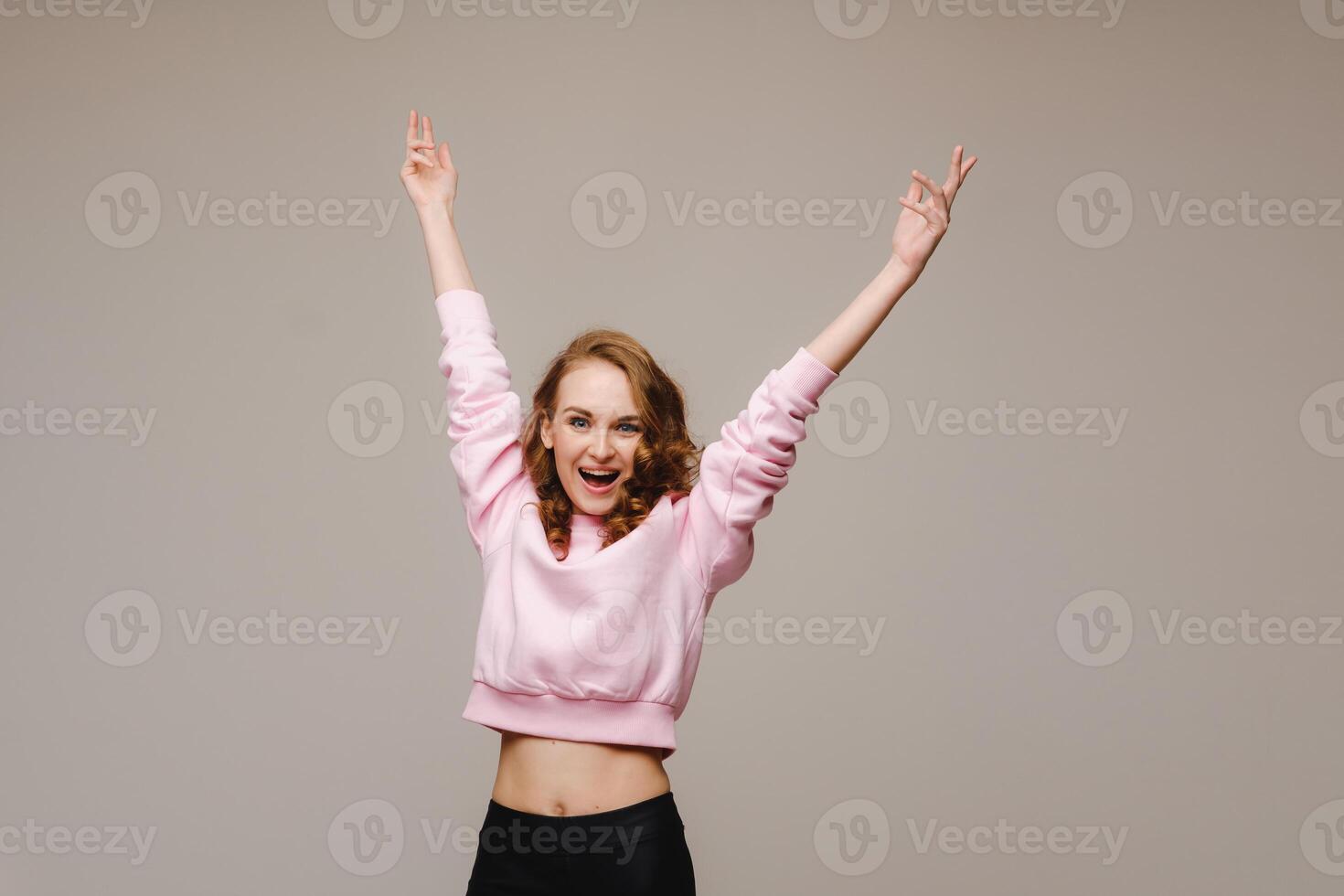 A beautiful emotional girl raises her hands up from happiness and what she sees on a gray background photo