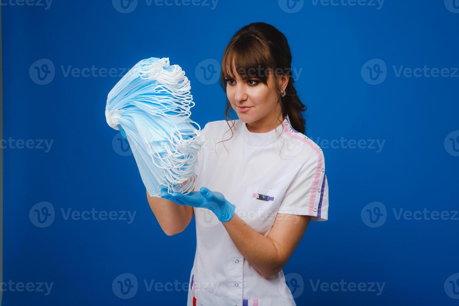 the doctor is holding a bunch of medical masks stacked together on a blue isolated background photo