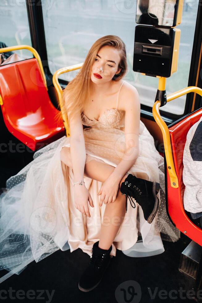 un novia en un Boda vestir con largo pelo paseos en el transporte de el ciudad de Breslavia. modelo novia sentado en un autobús asiento, Polonia foto