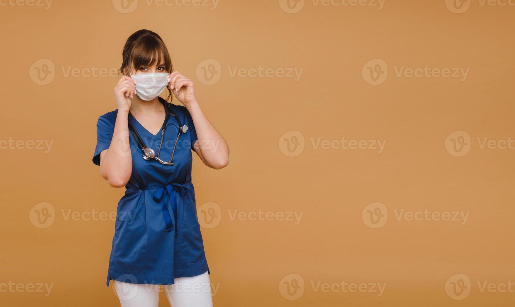 A girl doctor stands in a medical mask, isolated on a brown background photo