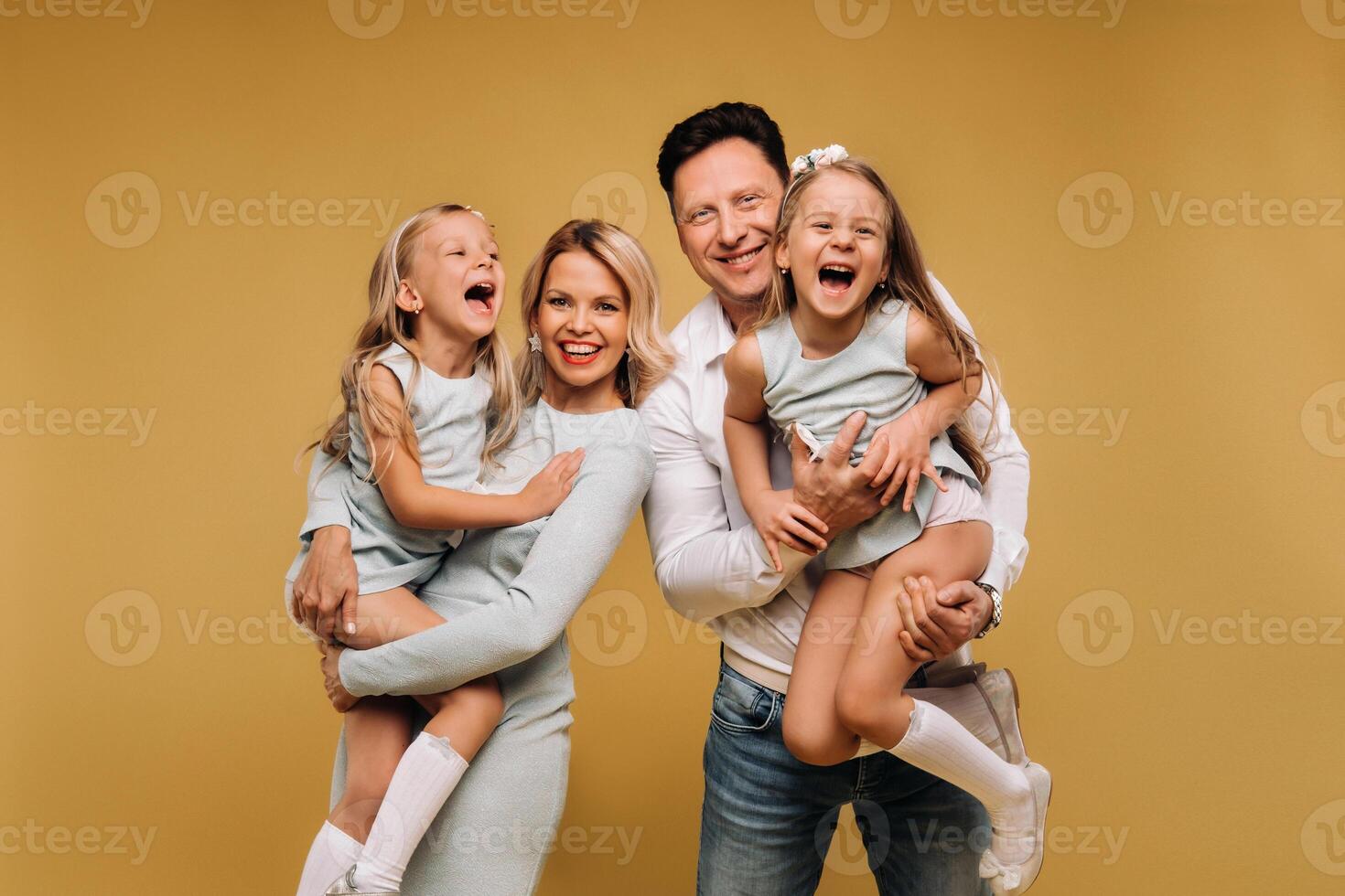 Happy parents hold their children in their arms and smile on a yellow background. an emotional family of four photo