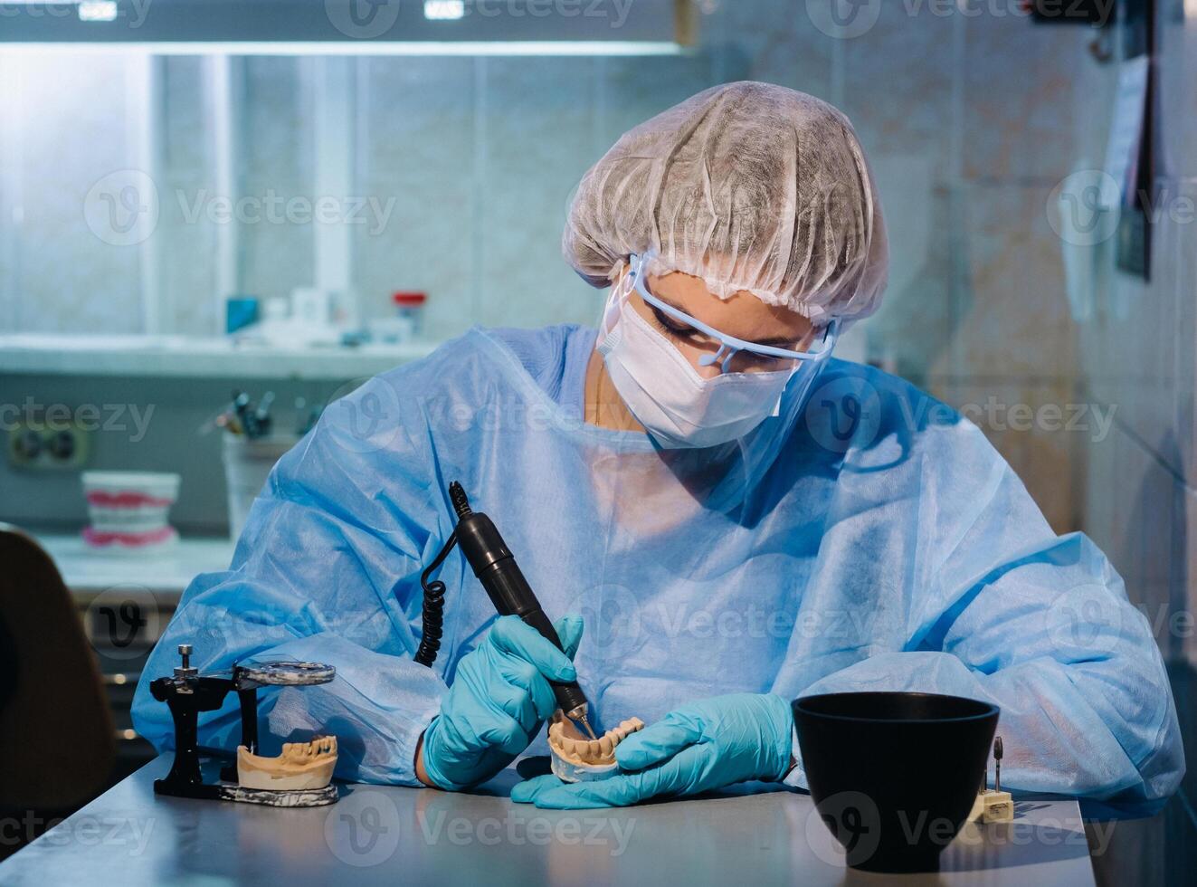 A masked and gloved dental technician works on a prosthetic tooth in his lab photo