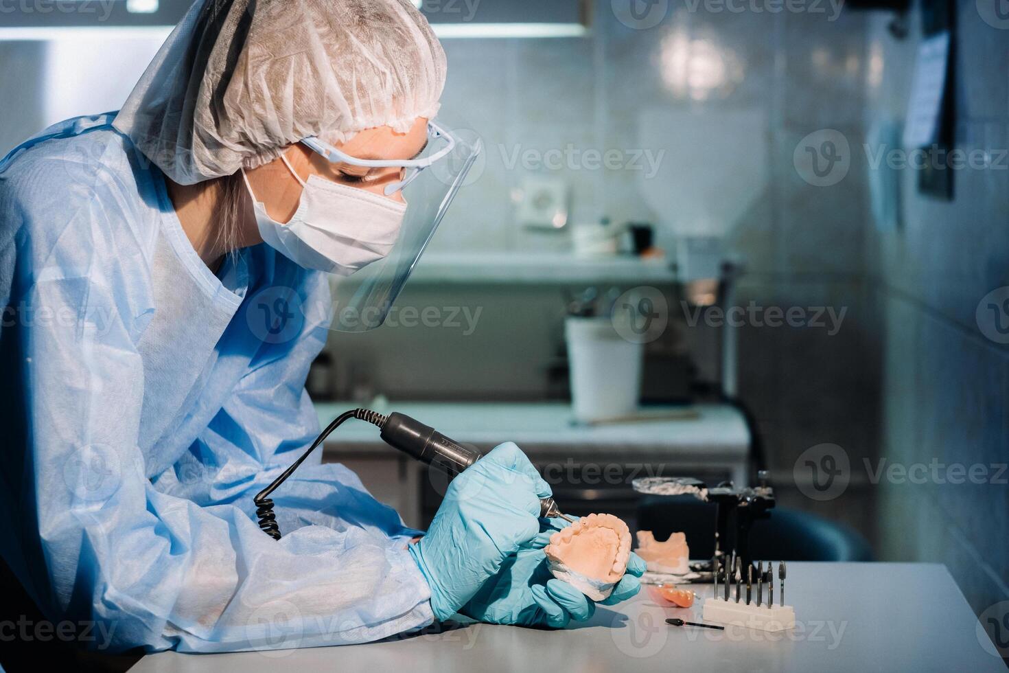A masked and gloved dental technician works on a prosthetic tooth in his lab photo