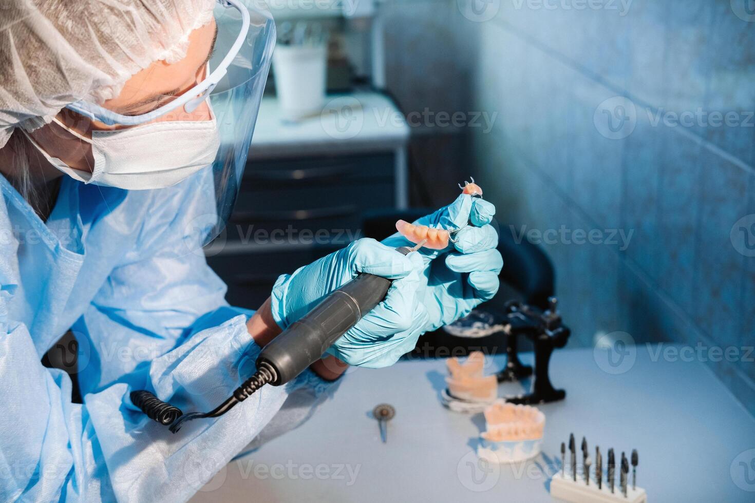 A masked and gloved dental technician works on a prosthetic tooth in his lab photo