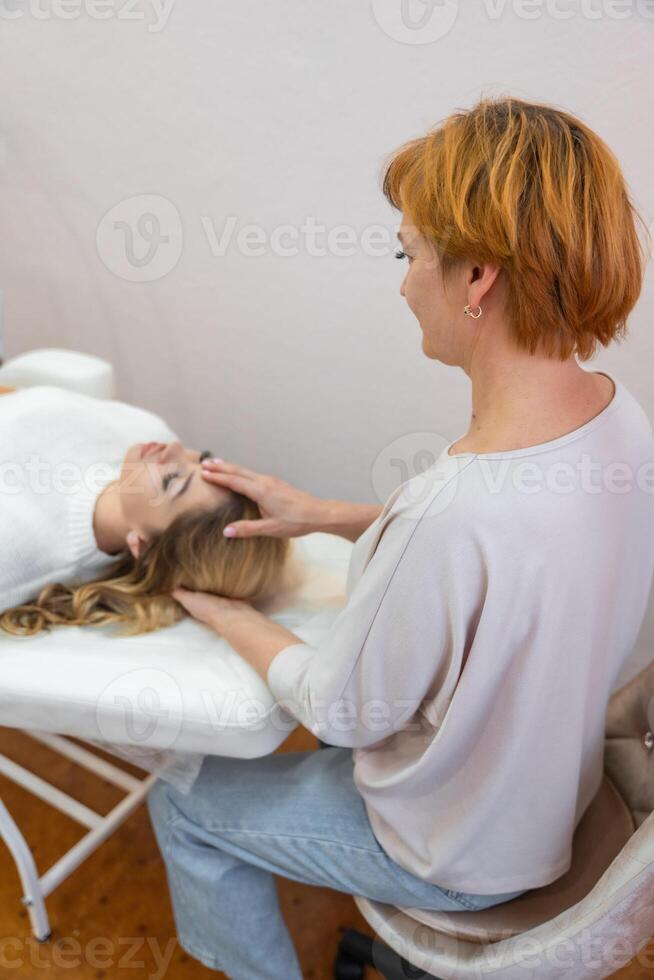 Healer woman performing by lightly touched set of 32 points of access bars on young woman head, stimulating positive change thoughts and emotions. Alternative medicine photo