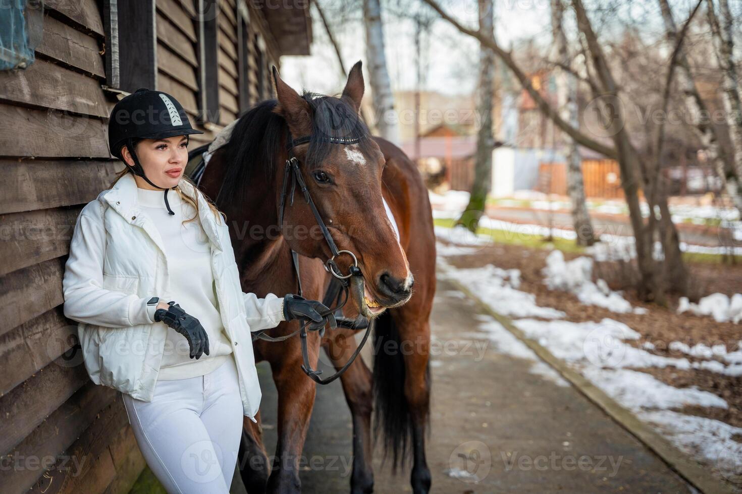 elegante rubio profesional hembra jockey en pie cerca caballo en granja. amistad con caballo foto