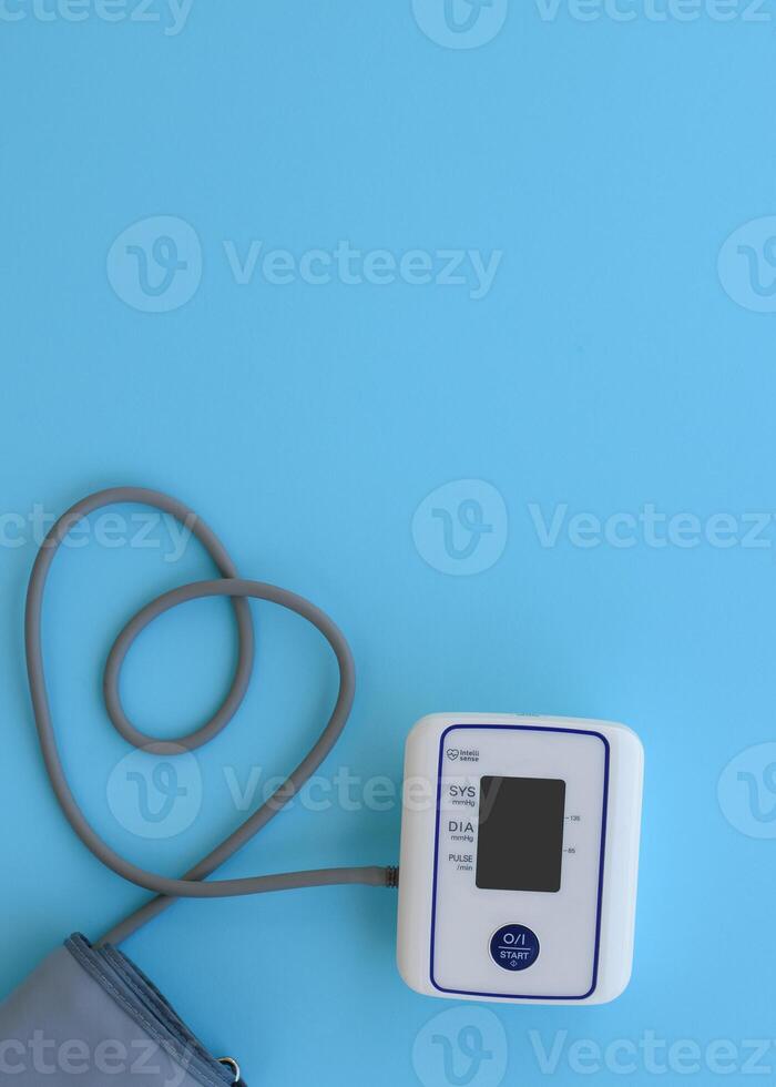 Automatic device for measuring blood pressure with heart from a tonometer cord on a blue medical background. Headache, treatment of hypertension and hypotension. Copy space vertical. Medical concept. photo