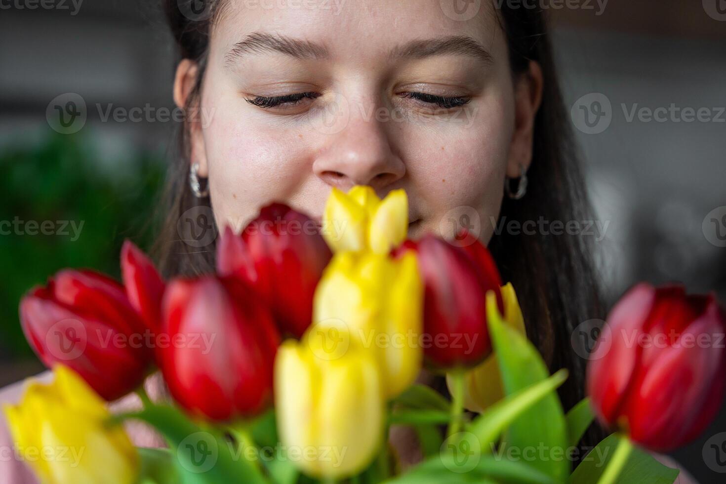 cerca arriba ver de cara de disfrutando joven mujer con un ramo de flores de rojo y amarillo tulipanes a hogar. Felicidades y un regalo en internacional De las mujeres día o de la madre día foto