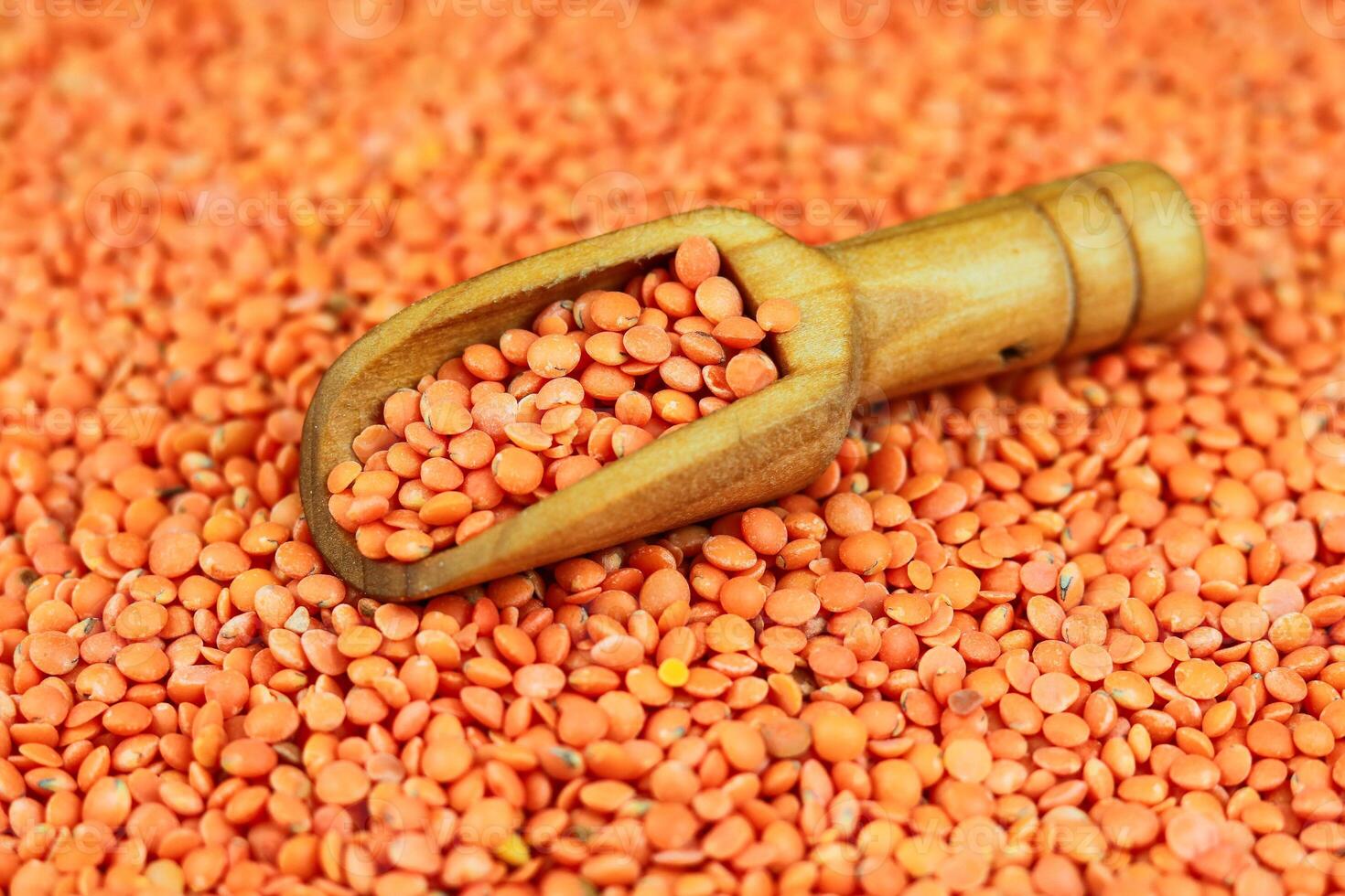 Red lentils in a wooden scoop on a background of red lentils photo