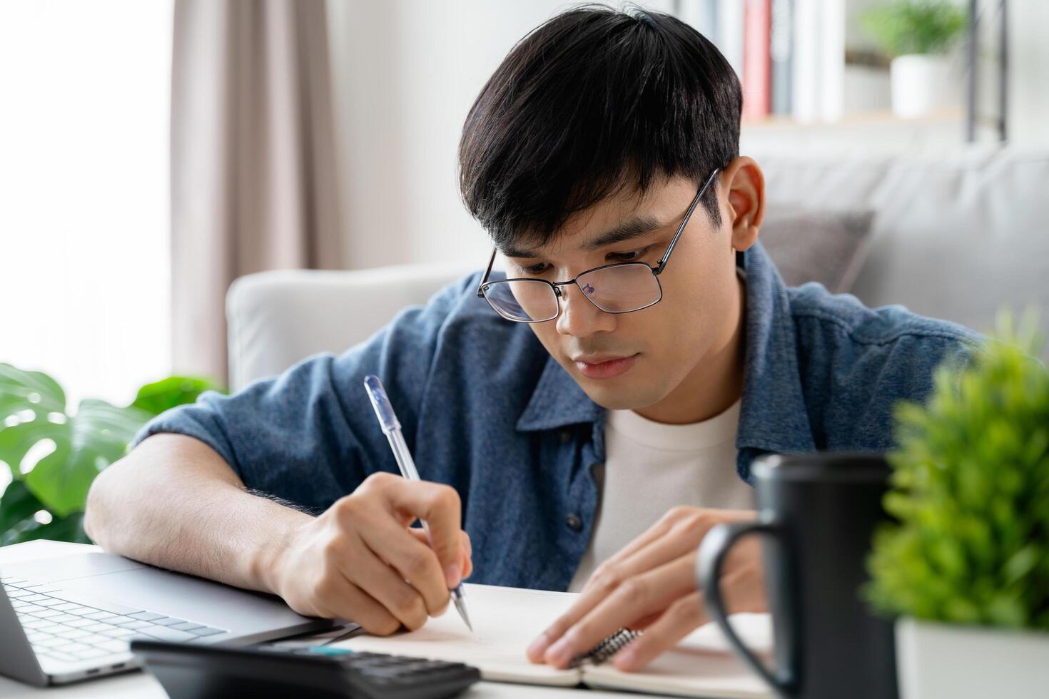 the man in casual clothes working with a laptop, computer, smart phone, calculator sitting on the sofa in the living room at home, working from home concept. photo