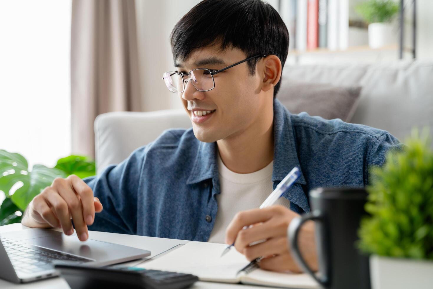 the man in casual clothes working with a laptop, computer, smart phone, calculator sitting on the sofa in the living room at home, working from home concept. photo