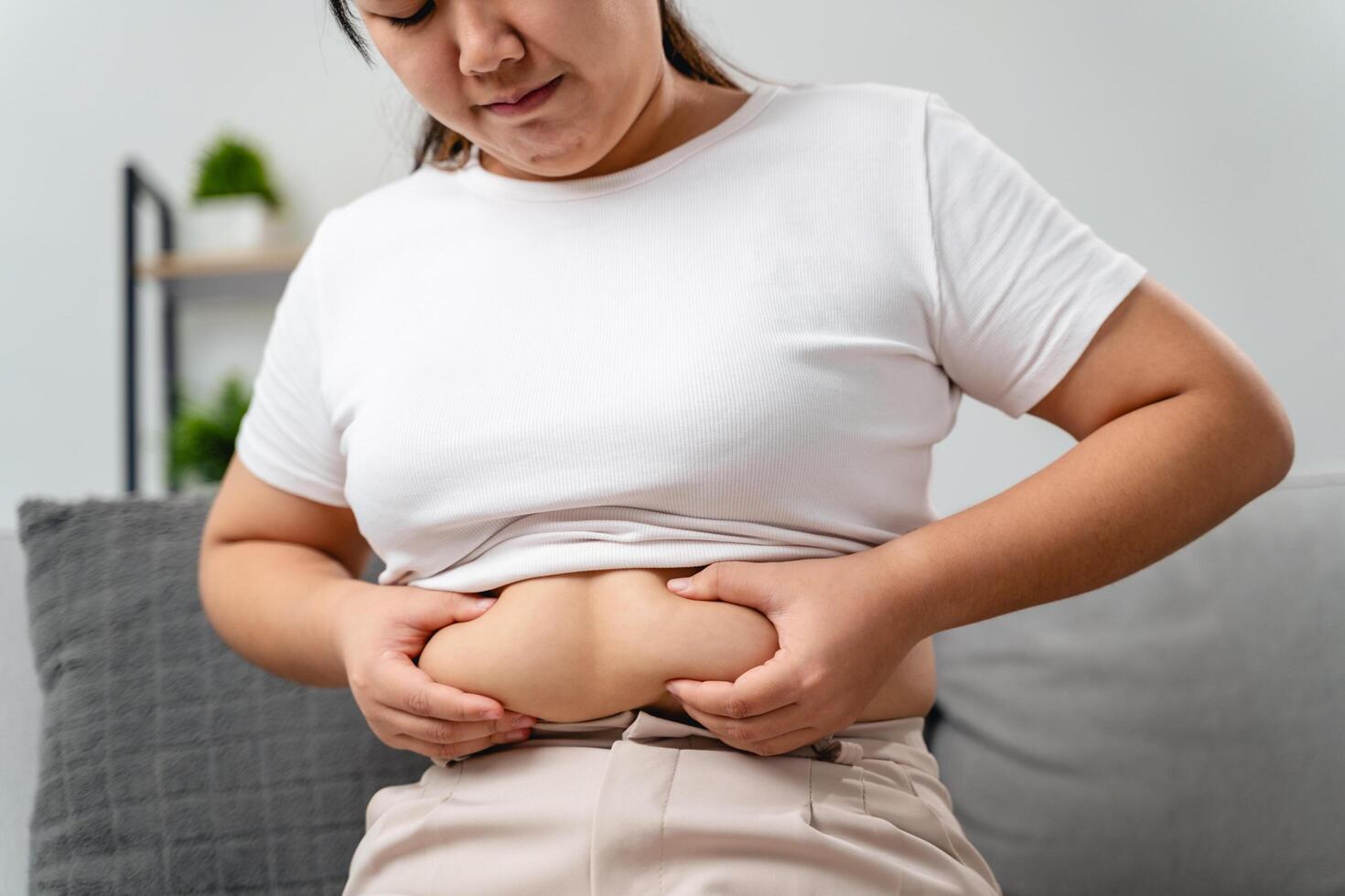 A woman is sitting on a couch and holding her stomach photo