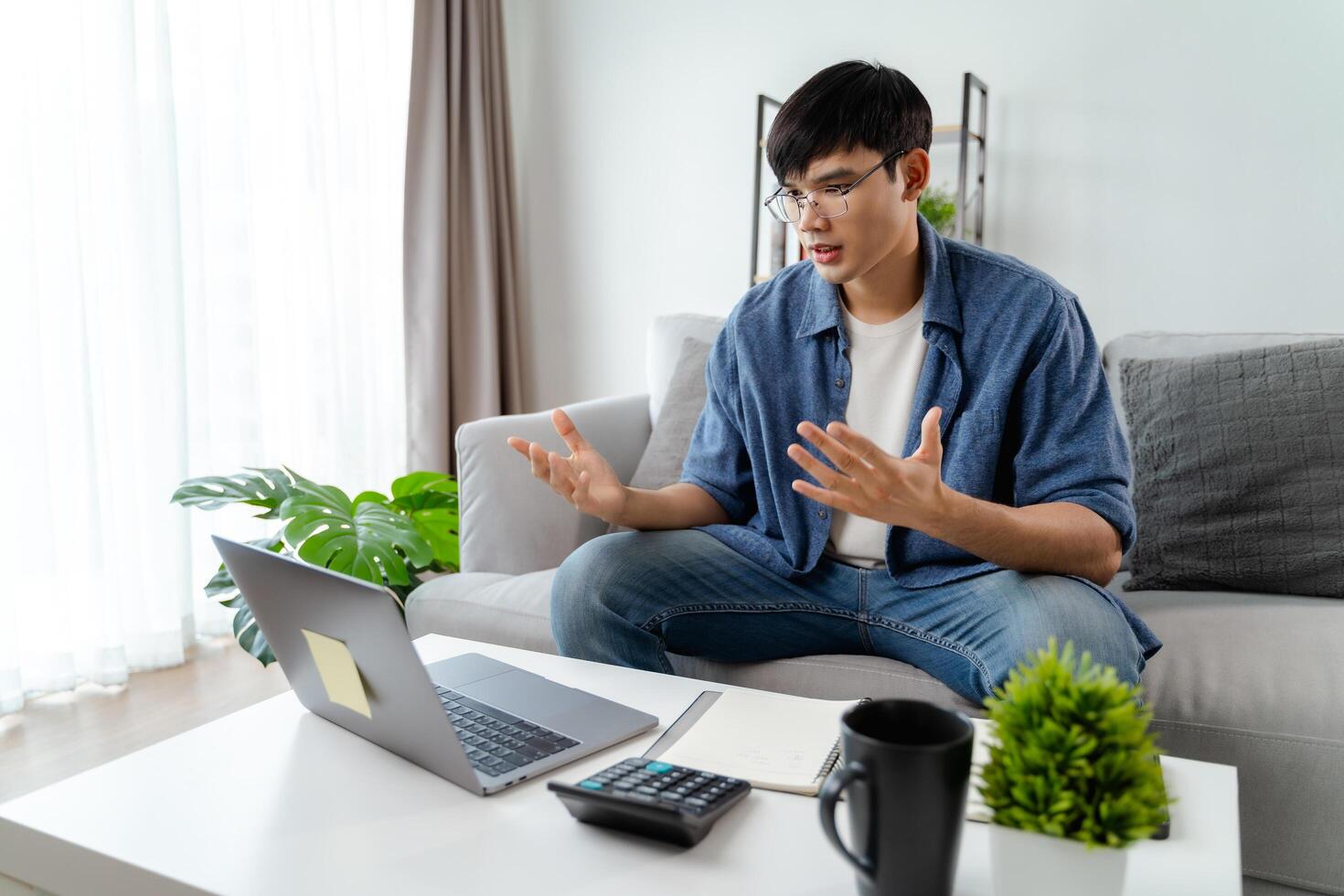 the man in casual clothes working with a laptop, computer, smart phone, calculator sitting on the sofa in the living room at home, working from home concept. photo