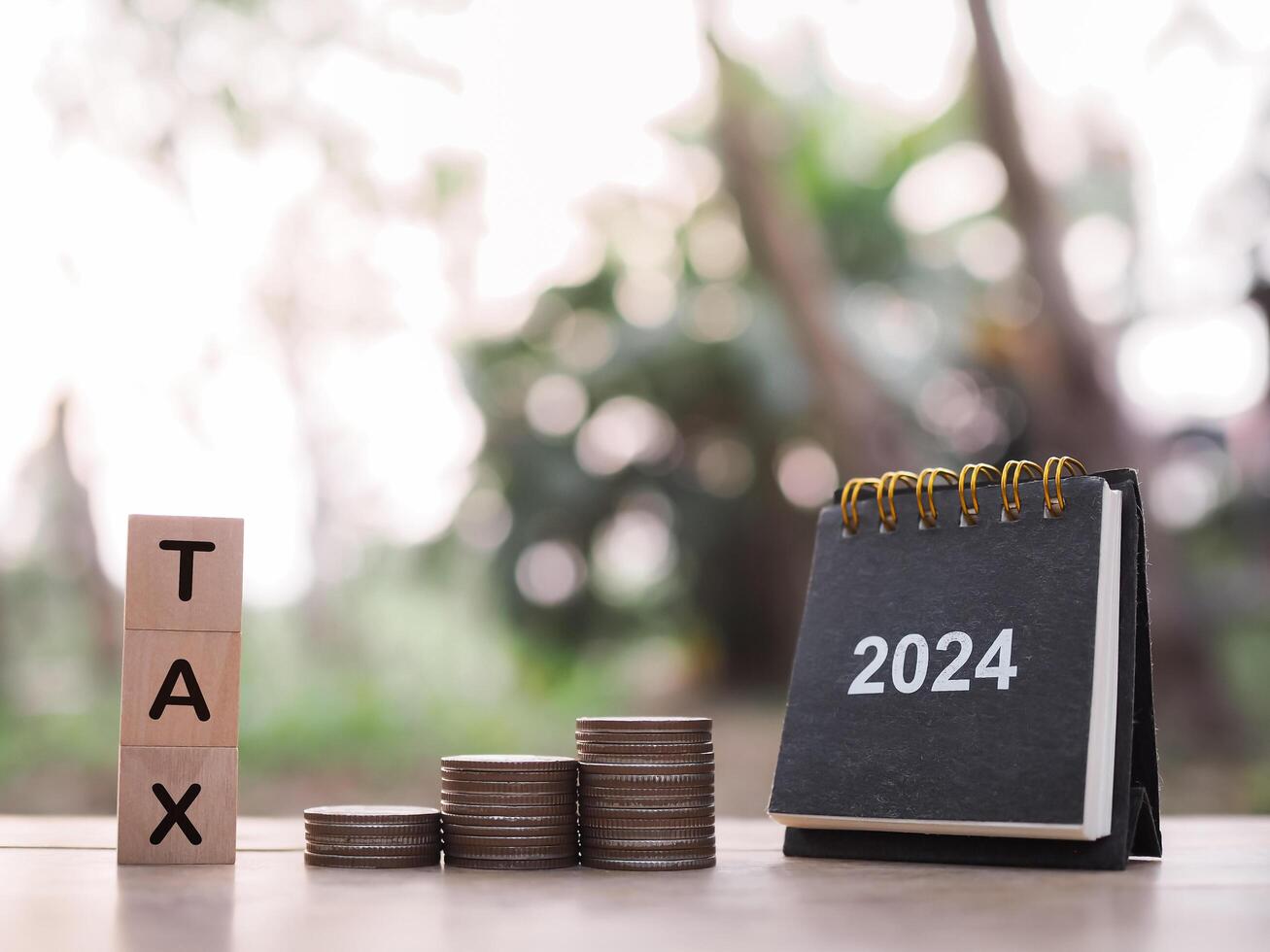 2024 desk calendar, Wooden block with word TAX and stack of coins. The concept of saving money for payment tax, Financial, Investment and Business growing in year 2024. photo