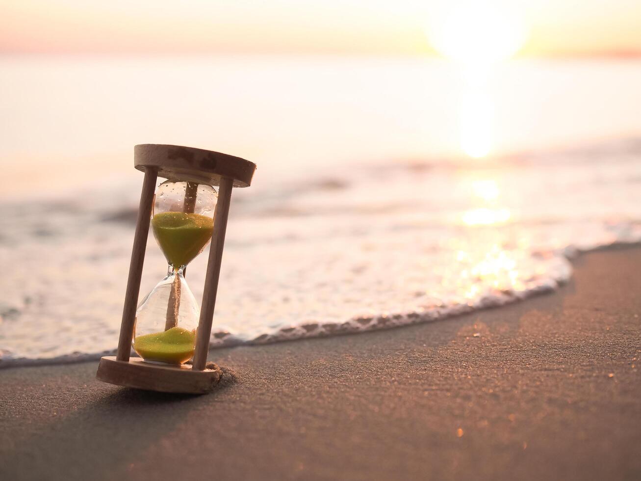 reloj de arena en el playa en el puesta de sol tiempo. el concepto acerca de cuenta regresiva a verano, viajar, vacaciones y relajación. foto