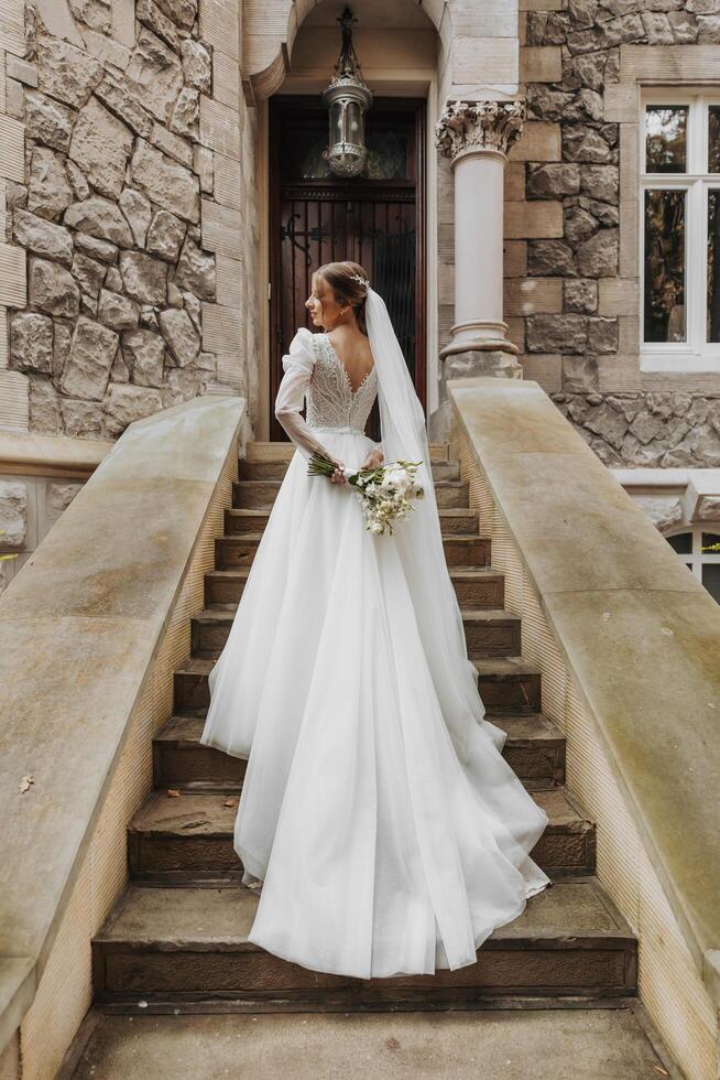 A bride in a dress climbs the stairs. Beautiful lady in a luxurious dress. Graceful bride. The bride climbs the stairs, a dress with a long train photo