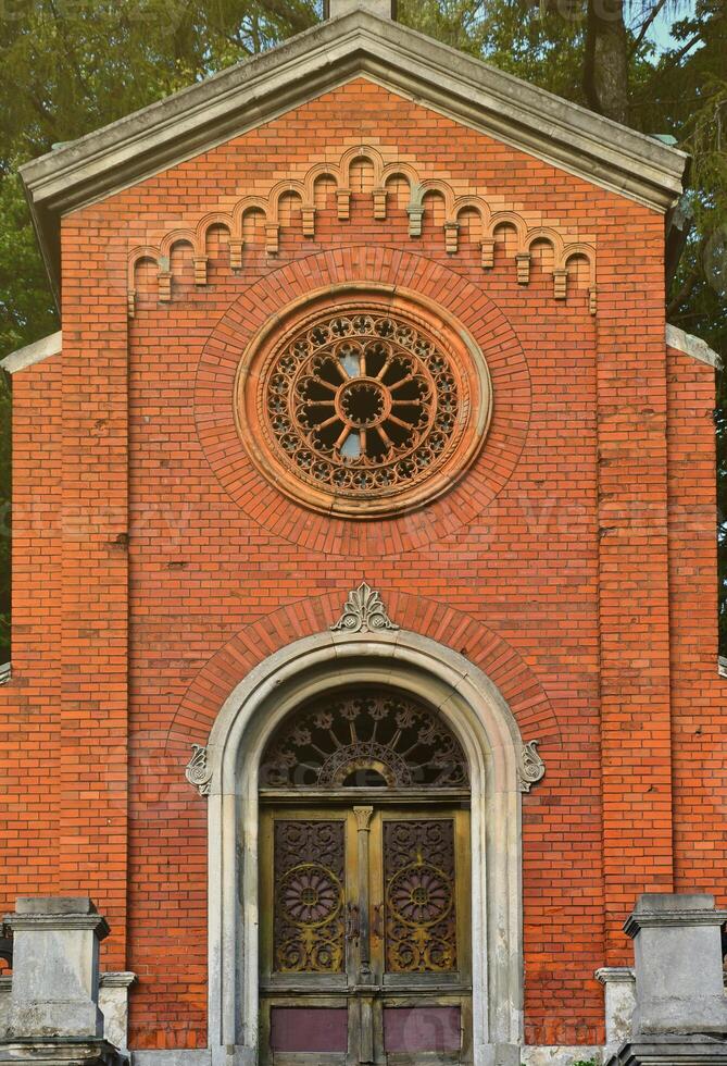 Texture front part of an ancient brick crypt with a round patterned carved window and a wooden door to the cemetery photo