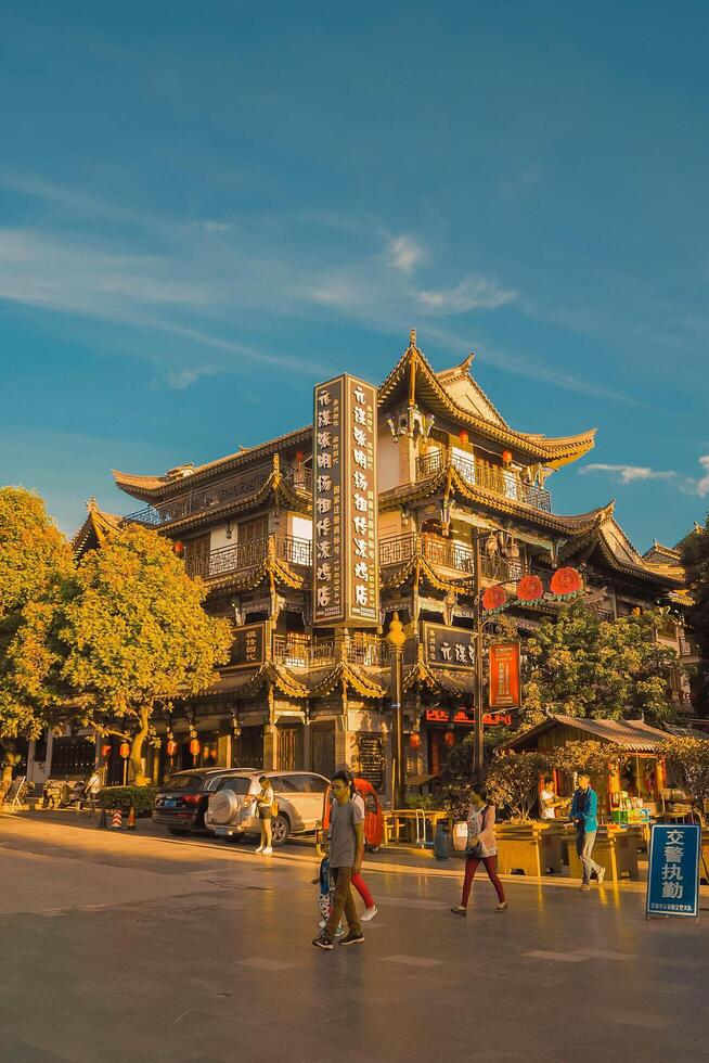 Yunan, China, 2016 - Aerial photograph of the landscape of an ancient Chinese city. People walk past the modern structure nestled between the Chinese-style and cement buildings during the golden hour. photo