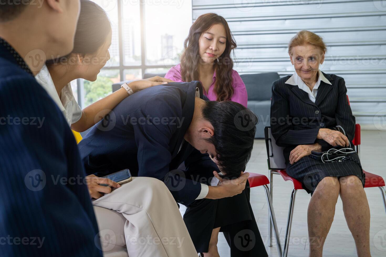 un grupo de personas son sentado en sillas, uno de quién es llanto. el otros son consolador él foto