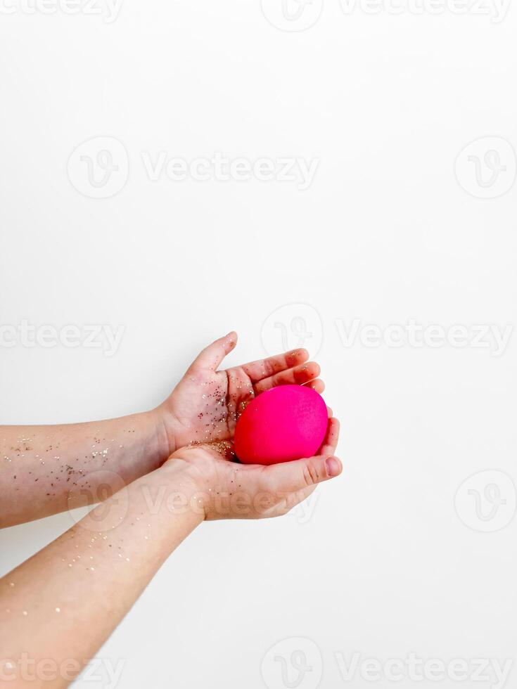 Hands holding a pink egg with glitter, Easter preparation and festive activity concept on a white background with copy space. For Easter themed creative content, and family activity ideas. photo