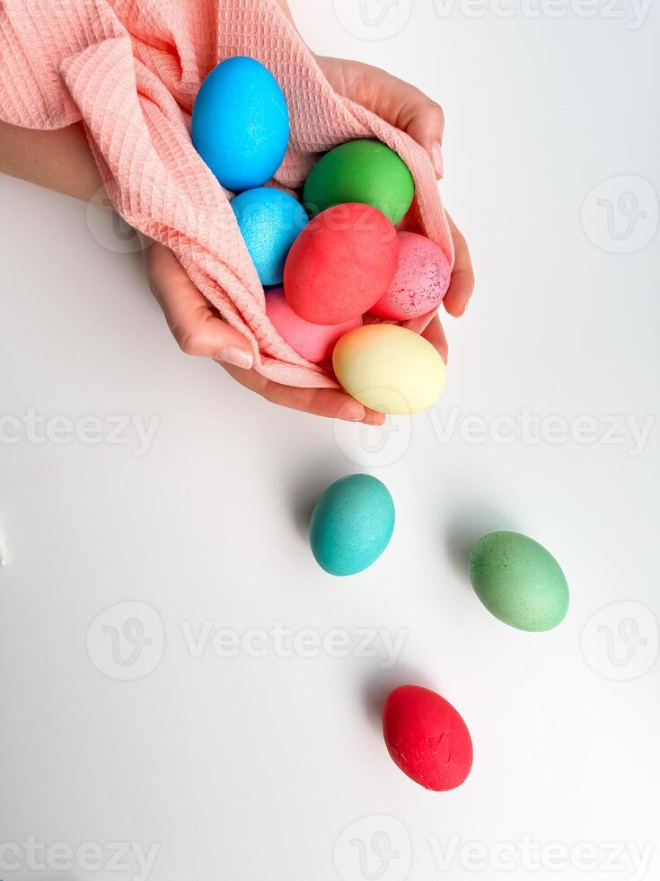 Hands cradling collection of brightly colored Easter eggs in pink fabric, evoking themes of Easter traditions, family fun, and springtime crafts. photo