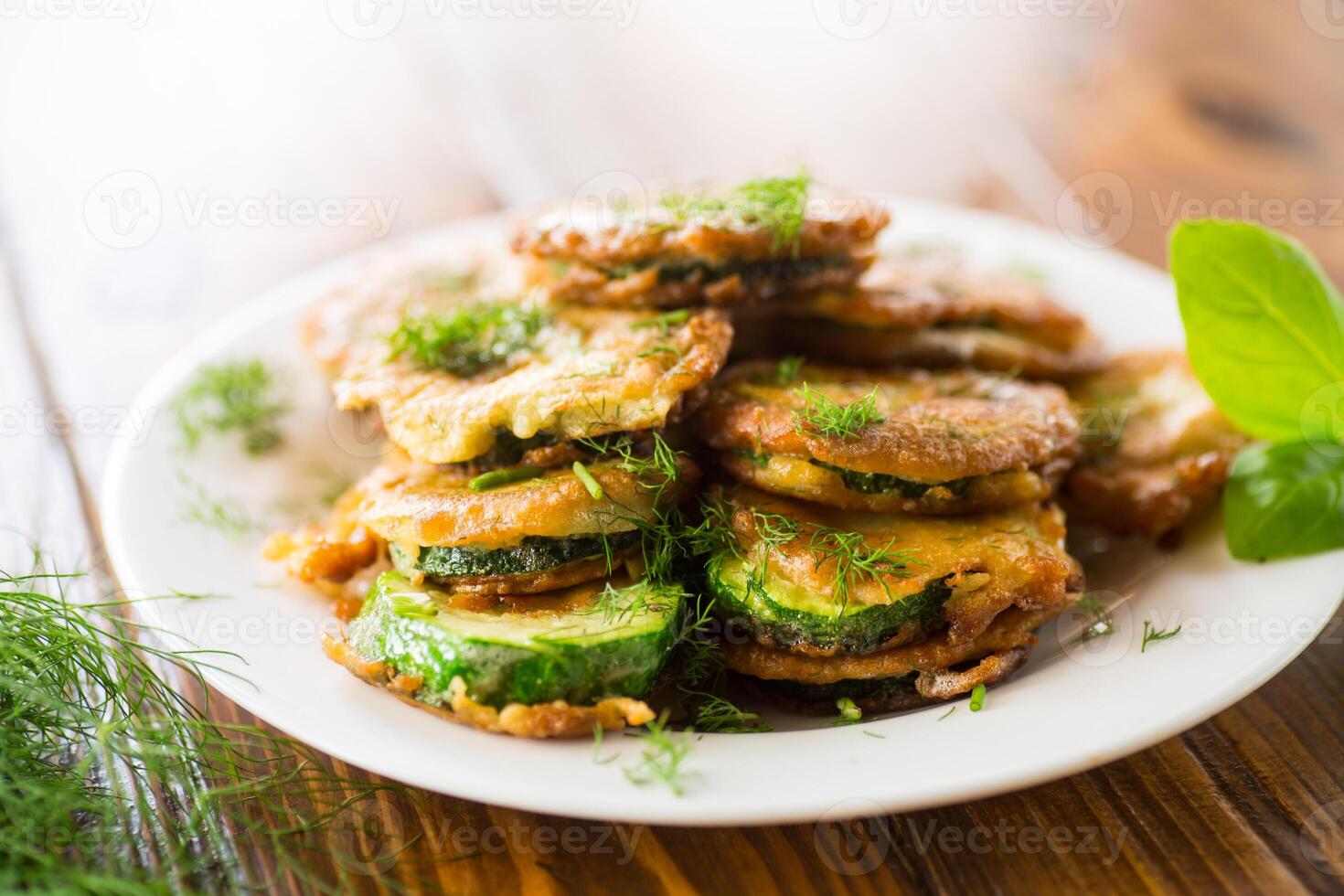 zucchini fried in circles in batter with herbs, in a plate . photo