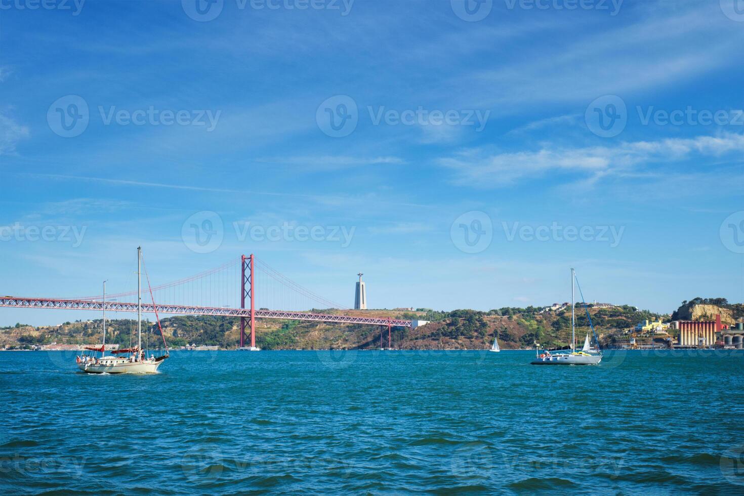 View of 25 de Abril Bridge over Tagus river, Christ the King monument and a yacht boat. Lisbon, Portugal photo