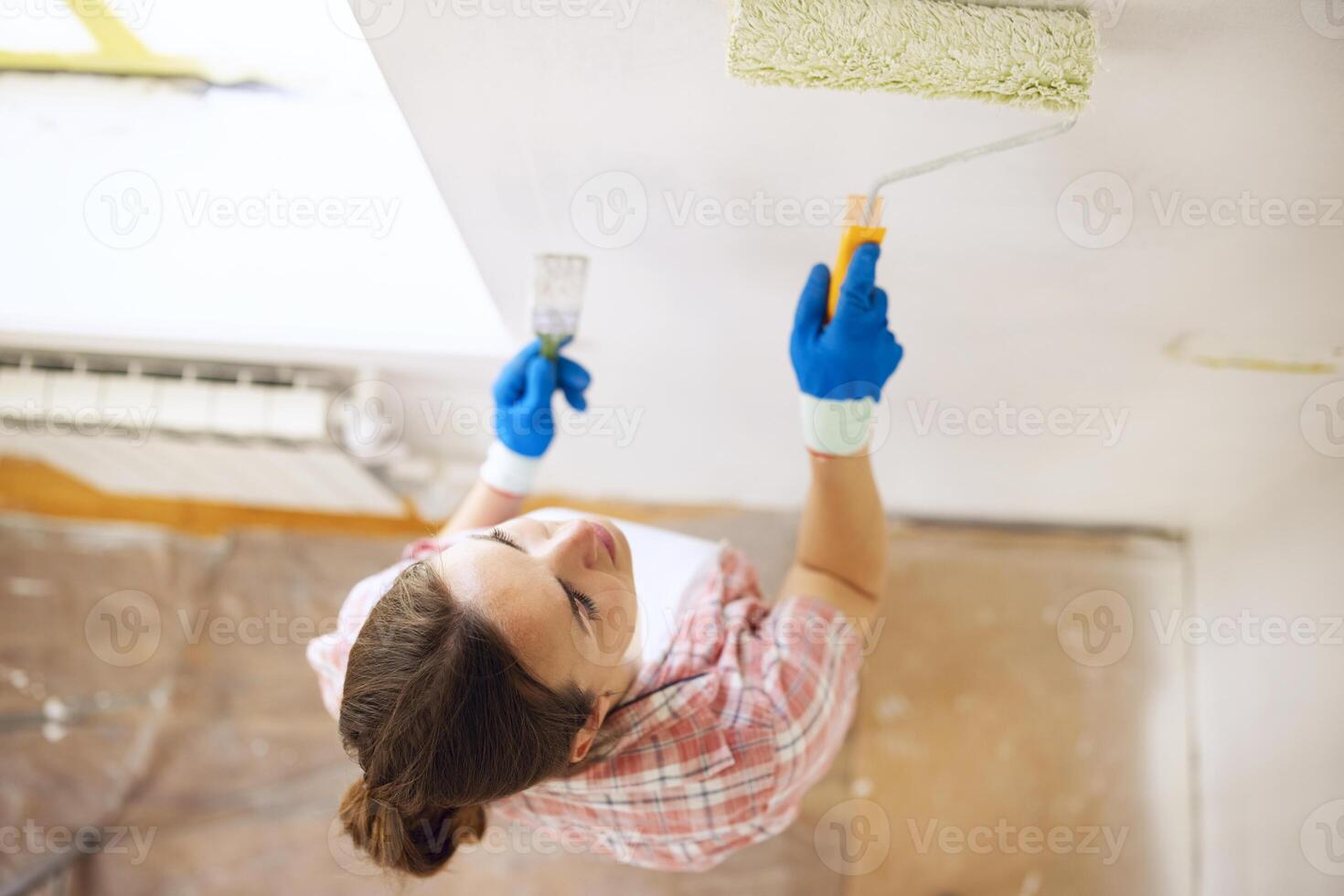 Smiling young woman with paint roller and brush paints walls in her apartment photo