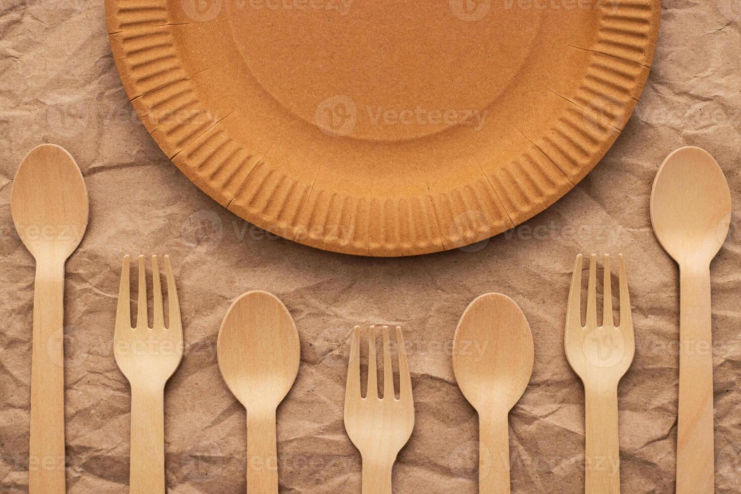 Wooden forks and spoons and paper plate on crumpled paper photo