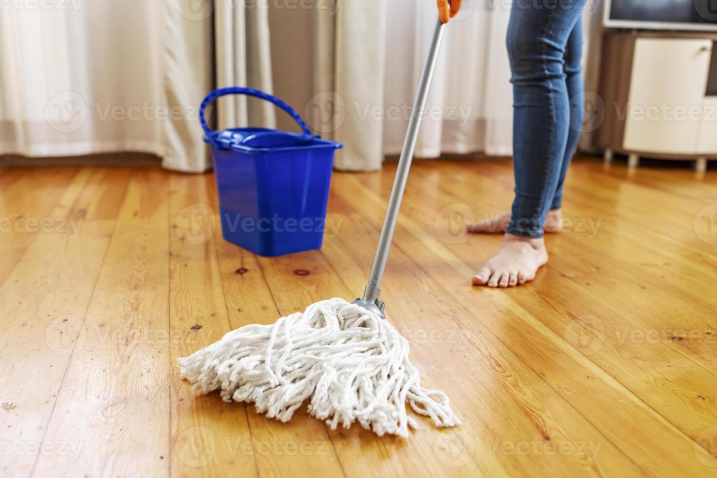 Young woman in protective gloves washing a wooden floor with a mop photo