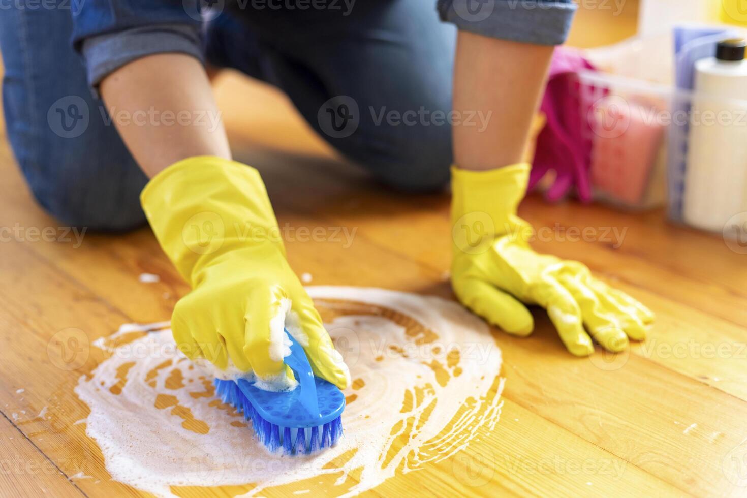 A young woman in protective gloves washes the floor with a brush and detergent photo
