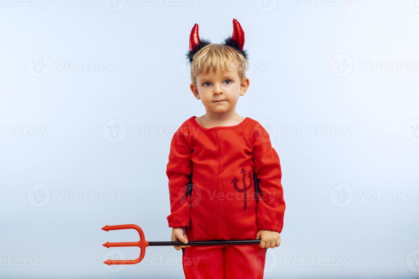 Happy cheerful boy in devil costume with trident on blue background photo